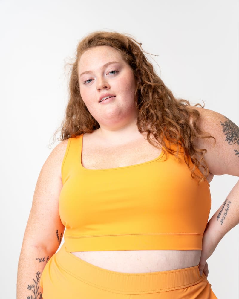 Front of a model wearing a size XL adventure cropped tank top in tangerine by alder apparel. | dia_product_style_image_id:349224